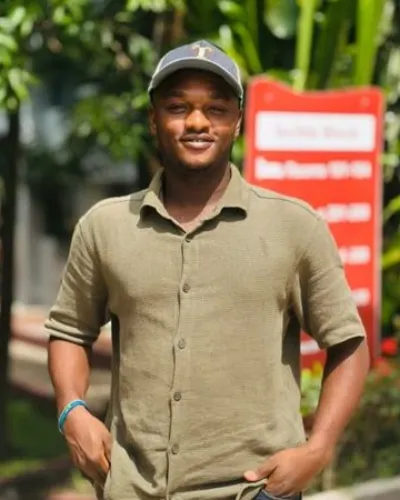 Portrait of Samuel Ghartey Anku in a green shirt and cap, smiling outdoors